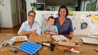 Auf dem Bild sieht man Yvonne Willicks und Natalie und Lenny Droste mit vielen verschiedenen Weihnachtsplätzchen.