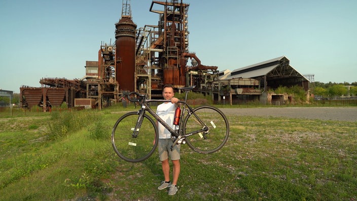 Ein Mann hält ein Rennrad am ausgestreckten Arm hoch