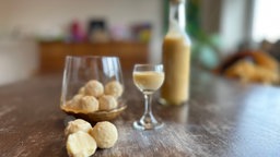 Eierlikörpralinen in einem Glas neben Eierlikör in Flasche und Glas