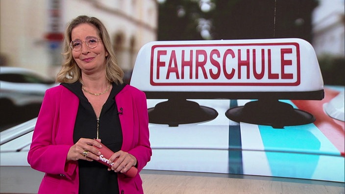 Yvonne Willicks steht im Servicezeit-Studio. Im Hintergrund ist ein Fahrschulauto abgebildet.