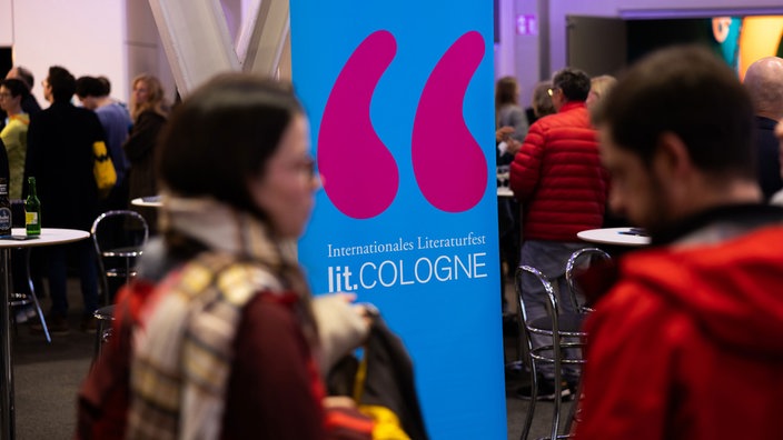 Besucher der Lit.Cologne vor dem Logo des Festivals