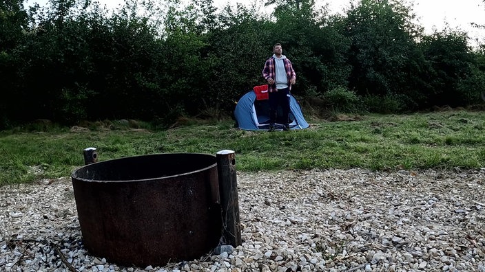 Ramon steht vor einem kleinen Zelt, im Vordergrund eine Feuerstelle