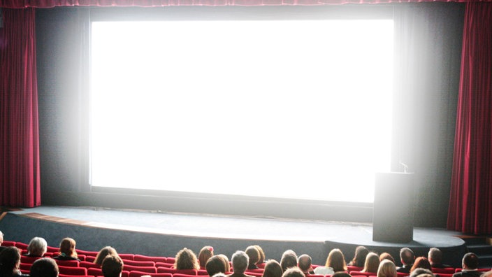 Publikum im Kinosaal vor weißer Leinwand