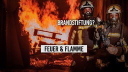 Zwei Feuerwehrleute vor brennenden Paletten