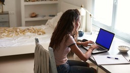 Eine junge Frau sitzt am Schreibtisch und tippt in ihr Notebook.