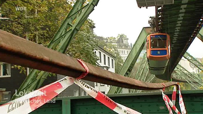 Heruntergefallene Stromleitung auf dem Boden, im Hintergrund eine hängende Schwebebahn.