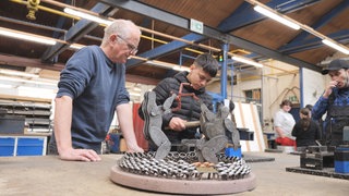 Schüler und Lehrer in einer Werkstatt, im Vordergrund ein Modell des Mahnmals des Solinger Brandanschlags.