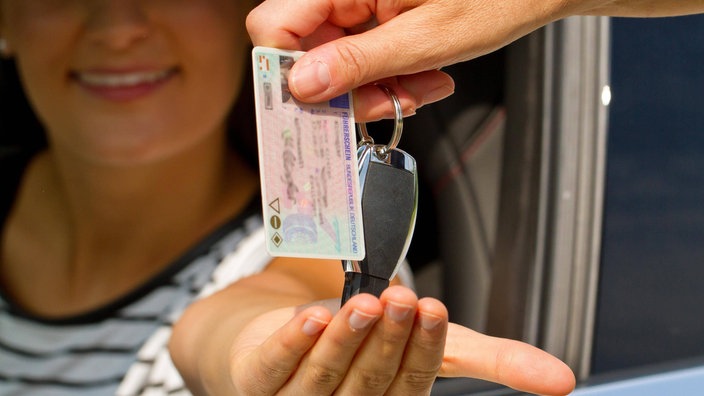 Frau bekommt Führerschein und Autoschlüssel ausgehändigt