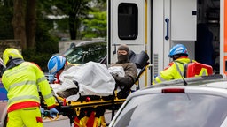 Ein verletzter Polizeibeamter wird vor einem Hochhaus in einen Krankenwagen gebracht