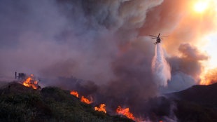  Ein Hubschrauber wirft Wasser auf das sich ausbreitende Feuer in Los Angeles