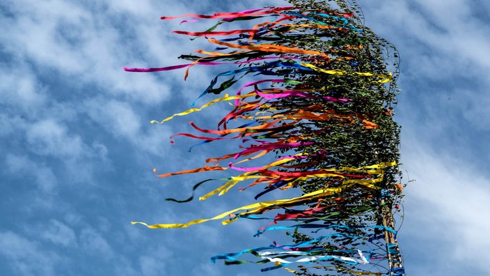 Köln: Bunte Bänder eines Maibaumes flattern vor dem blauen Himmel.