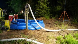 Ein blaues Plastikschwimmbecken steht auf einem Waldboden. Feuerwehrschläuche führen heraus.