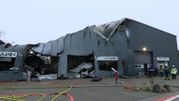 Auf dem Foto ist eine Halle, deren Wände geschmolzen und eíngefallen sind. Das Logo der Firma ist noch sichtbar.