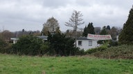 Das Haus des Klägers von der Wiese aus, mit einem riesigen Plakat und der Aufschrift : "Wir klagen!"