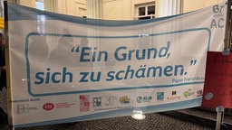 "Ein Grund sich zu schämen" steht auf einem Banner bei der Demo gegen Bischof Dieser in Aachen