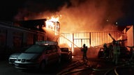 Großbrand im Dunklen im Hintergrund, im Vordergrund löschende Feuerwehrleute