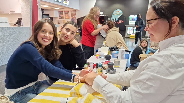 Zwei Schülerinnen lassen sich auf Pflegemesse an einem Stand massieren