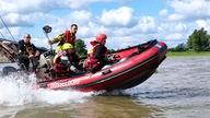 Auf dem Foto ist ein rotes Feuerwehrboot mit vier Männern darauf. Neben dem Boot schäumt das Wasser.