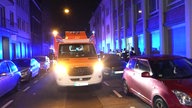 Auf dem Foto ist ein Rettungswagen, der mitten auf der Straße steht, rechts daneben auf dem Gehweg stehen Rettungssanitäter und Feuerwehrleute.