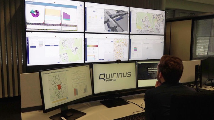 Ein Mann schaut im Elsdorfer Quirinus Center auf neun miteinander verbundene Computerbildschirme auf denen sich teils Stromnetze abbilden.