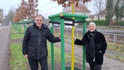 Ein Mann und eine Frau stehen an einem frisch gepflanzten Baum