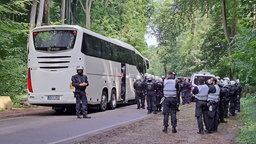 Polizisten stehen am Wegrand an einem Waldstück, im Hintergrund steht ein großer Bus.