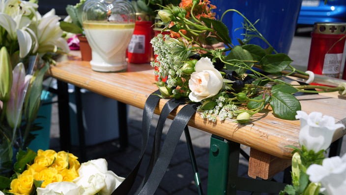 Blumen liegen mit einem schwarzen Trauerflor auf einer Holzbank