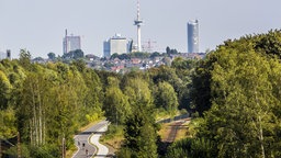 Die Essener Skyline hinter einem grünen Stück Landschaft mit einer Straße und Schienen 