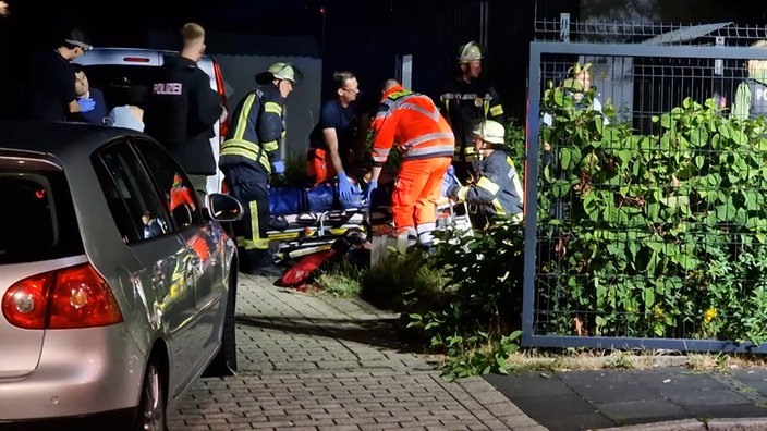 Rettungssanitäter und -sanitäterinnen beugen sich über eine verletzte Person, die auf einer Trage liegt.