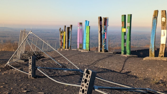 Holzstelen auf Halde Haniel mit umgestürztem Absperrungszaun vor den Totems