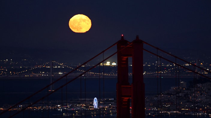 Hinter der Golden Gate Bridge ist am Himmel ein goldfarbener Vollmond zu sehen. 