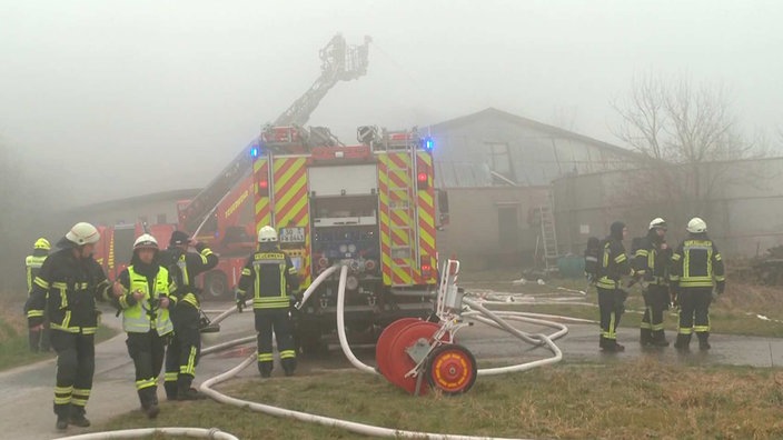 Ein Löschfahrzeug und Einsatzkräfte der Feuerwehr stehen vor einem brennenden Stall. 