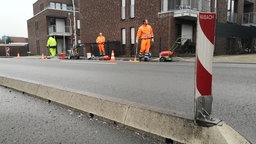 Es sind zu sehen 3 Bauarbeiter, die die Straße abflemmen