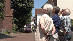 Mehrere ältere Menschen, die neben einer Kirche stehen und nach oben gucken