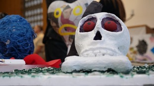 Ein Totenkopf auf Pappmarché mit roten Augen steht auf einem Tisch. 