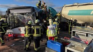 Feuerwehrleute untersuchen einen Lkw, der mit einem Bus zusammengekracht ist