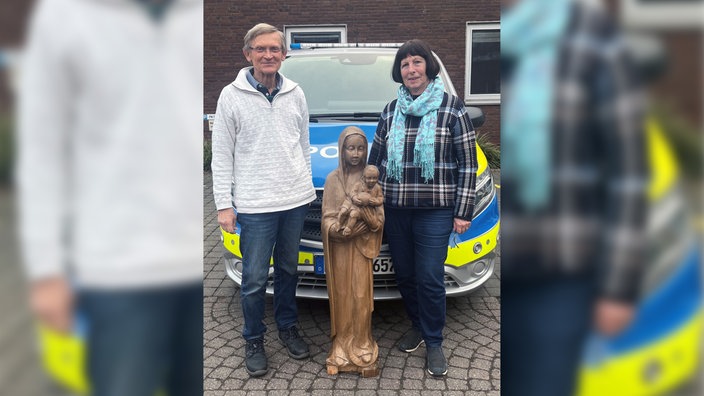 Madonna-Figur mit Besitzern vor Polizeiwagen.