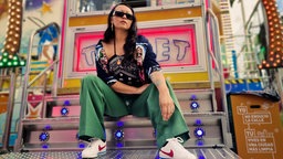 DJ Asia Knox auf der Treppe eines sehr bunten Kirmes Fahrgeschäfts