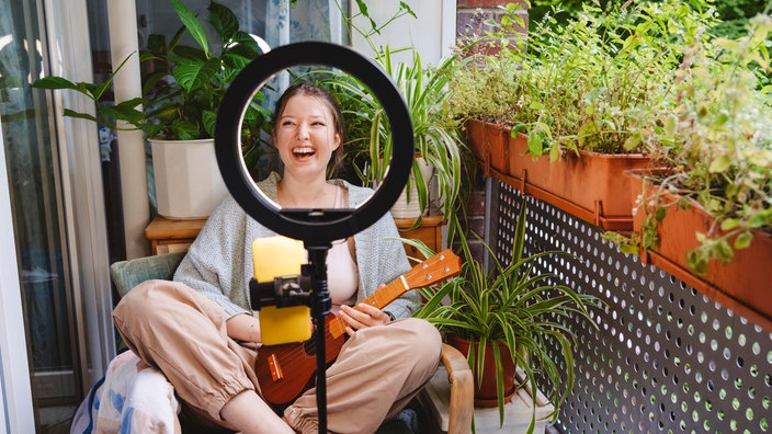 Fröhlicher Influencer mit Ukulele-Streaming-Online-Konzert auf dem Balkon