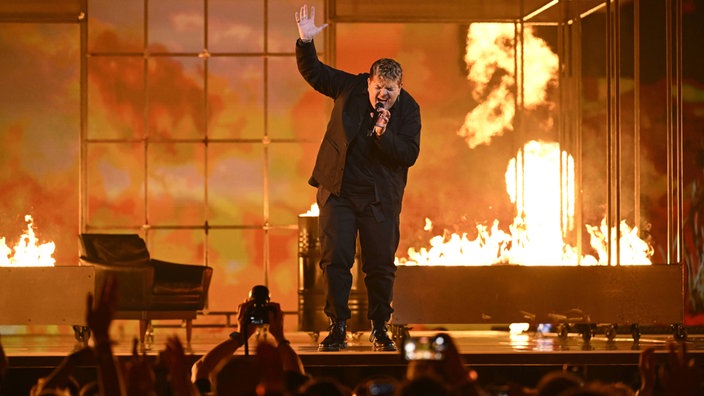 Isaak singt auf der Bühne beim Eurovision Song Contest 2024 vor Flammen und im hellen Lichtschein