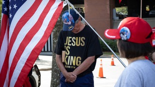 Evangelikaler Anhänger von Donald Trump betet mit T-Shirt Aufdruck "Jesus is King" neben einer USA-Flage