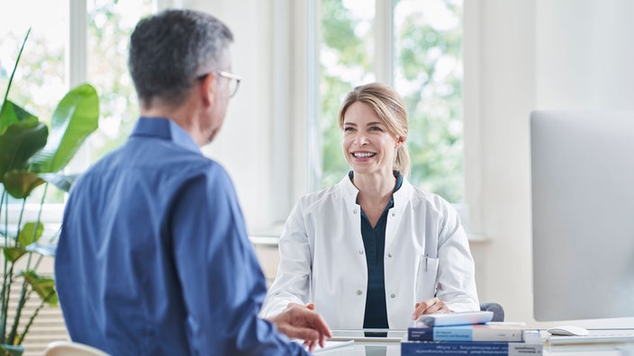 Lächelnde Ärztin sitzt mit einem männlichen Patienten am Tisch