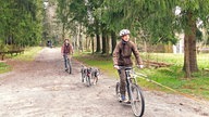 Zwei Mädchen auf dem Fahrrad mit Hunden