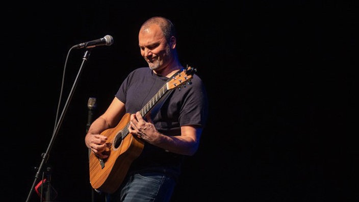 Danko Rabrenović performt mit Gitarre und Mikrofon auf einer Bühne.