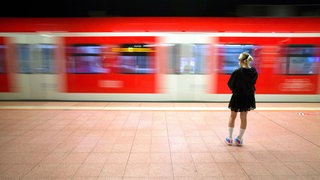 Junge Frau steht am Bahnsteig während ein Zug der Deutschen Bahn vorbeifährt. 