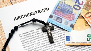 Symbolbild Kirchensteuer - Kreuz mit Euro Geldscheinen auf einem Brief mit der Aufschrift: Kirchensteuer.