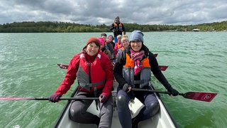 Acht Frauen und ein Mann in einem Paddelboot auf einem See