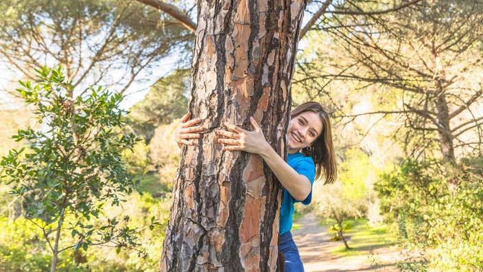 Frau die lachend einen Baum im Wald umarmt