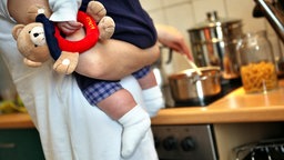 Eine Mutter hält beim Kochen ihr Kleinkind auf dem Arm