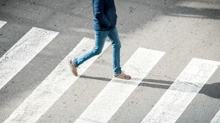 Ein Fußgänger in Jeans und Sneakern überquert einen Zebrastreifen.